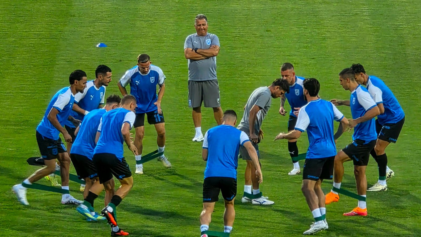 Soccer team doing a resistance-band warm-up on the field before practice.