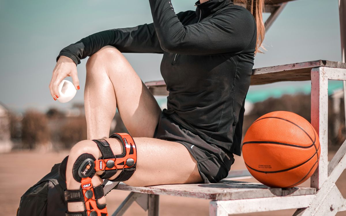 Athlete in a hinged knee brace sitting on the bleachers with a basketball.