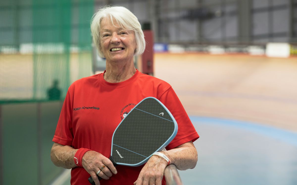 Smiling older woman holding a pickleball paddle.