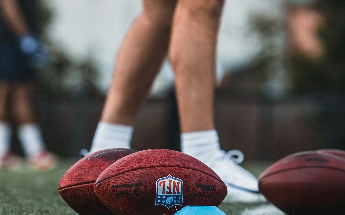 Footballs on a practice field next to a player's cleats.
