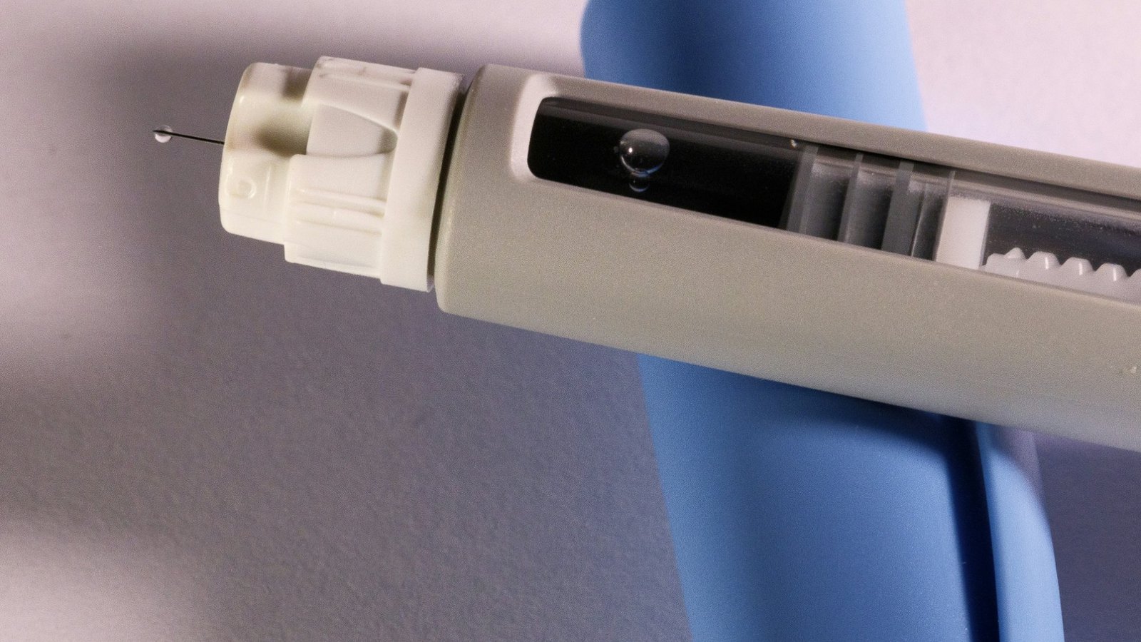 Close-up of a GLP-1 injection pen with a drop on the needle tip, resting on a second pen.