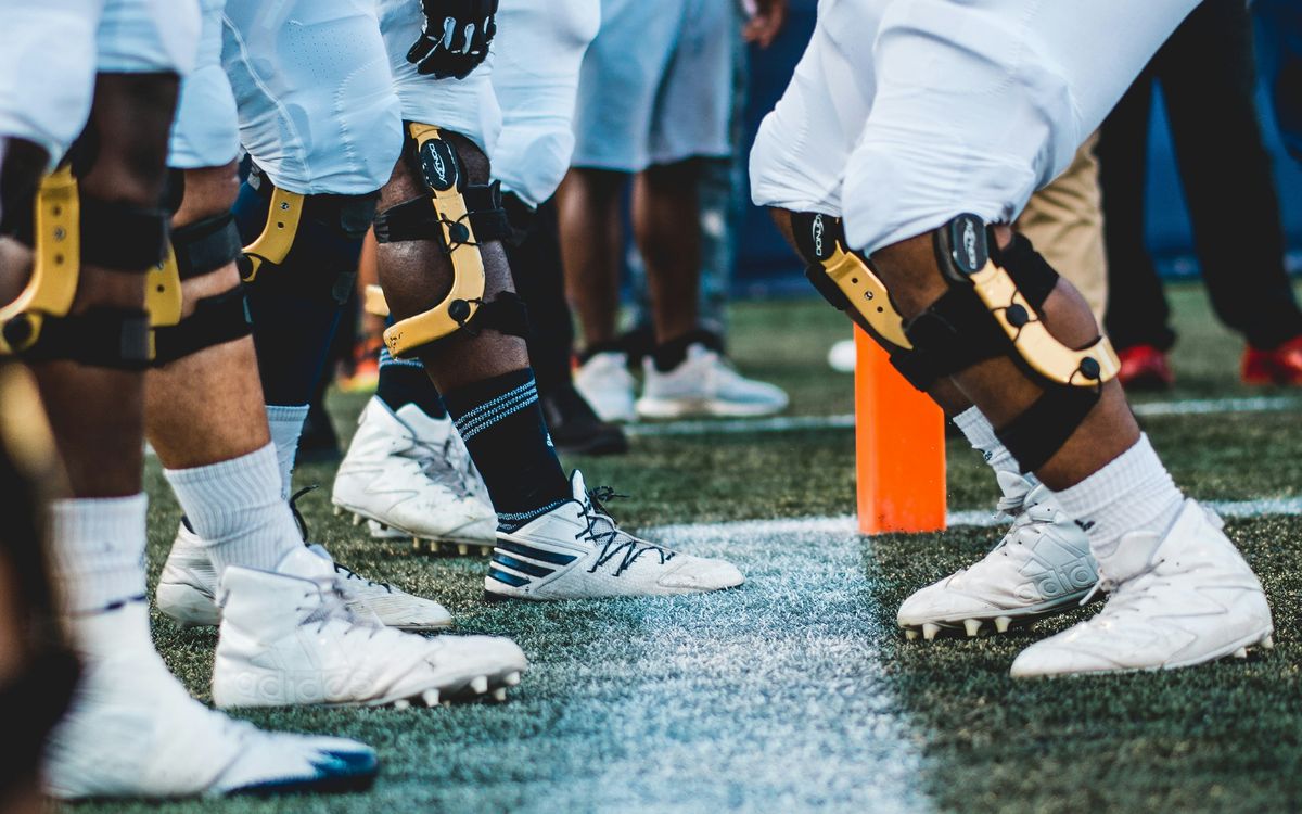 Football linemen wearing knee braces at the line of scrimmage.
